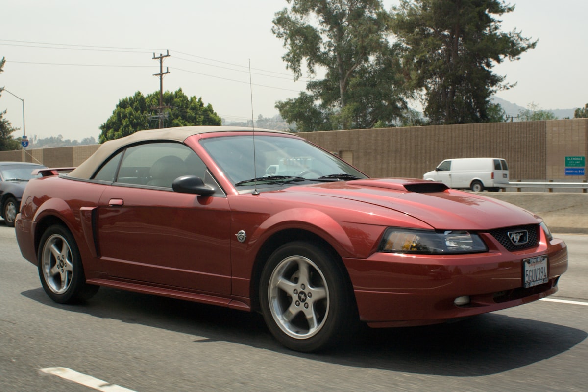 Red convertible top-down parked beside palm trees on a coastal road