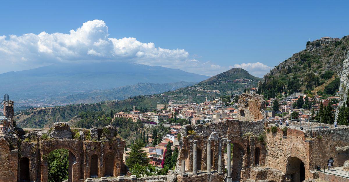 Car on a road in Sicily with the coast and ancient ruins in the distance
